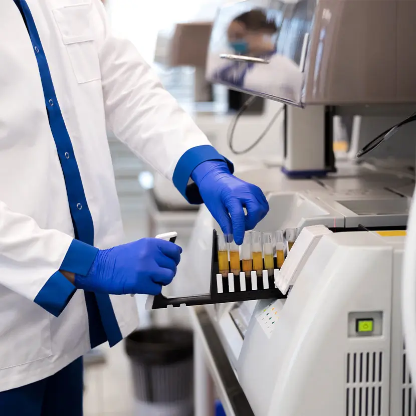 Hospital laboratory with automated analyzer and technician handling test tubes for sample processing