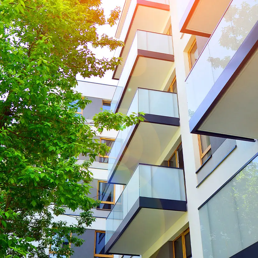 Modern building exterior with balconies and glass railings surrounded by green foliage for LEED compliance